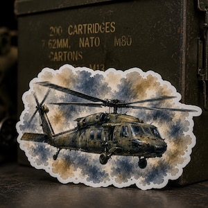 Könnte beinhalten: Ein gestanzter Aufkleber mit einer detaillierten Illustration eines Militärhubschraubers im Flug. Der Hubschrauber ist in Olivgrün- und Brauntönen gehalten und vor einem aquarellartigen Hintergrund aus blauen und beigen Wolken mit weißem Rand platziert.