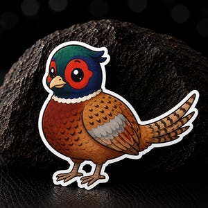 Op de afbeelding: Een gestanste sticker met een cartoonfazant met een donkergroene kop, felrode oogvlekken en een bruin lichaam met patronen. De vogel heeft grote zwarte ogen, een lichte snavel en een lange, gestreepte staart. De sticker heeft een witte rand.