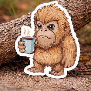 May include: A sticker featuring a cartoon Bigfoot with brown fur and blue eyes, holding a steaming blue mug. The Bigfoot has a serious expression. The sticker is placed on a natural wood background.