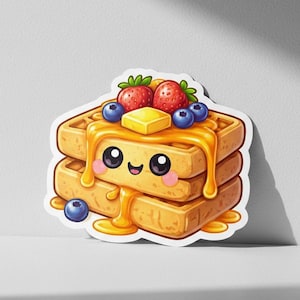 Puede incluir: Una pila de gofres de dibujos animados con una cara sonriente, cubierta con fresas, arándanos y una nuez de mantequilla. Se vierte jarabe de miel sobre los gofres. Los gofres son de color marrón claro.