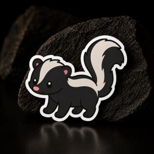 May include: A die-cut sticker featuring a cartoon skunk with black fur, a white stripe running from its head down its back, and a large, bushy, black and white tail. The skunk has a small pink nose, rounded ears, and large black eyes.