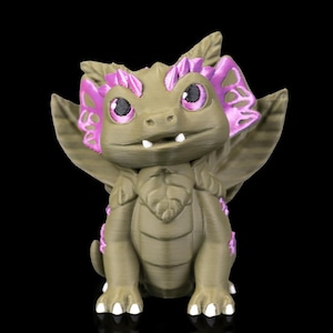 May include: A 3D-printed figurine of a friendly-looking dragon. The dragon is primarily olive green with pink accents on its wings and head. It has large, round eyes and small white teeth. The figurine is set against a black background.
