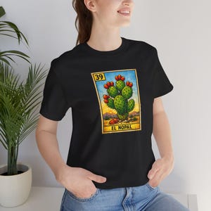 May include: Black t-shirt featuring a colorful graphic of a cactus with red fruit, set against a desert landscape. The image includes the number "39" and the text "EL NOPAL" in a vintage style.