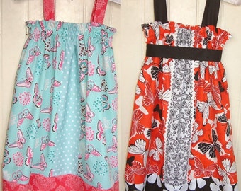 Puede incluir: Dos vestidos sin mangas para niñas con estampados de mariposas. El vestido de la izquierda es turquesa con lunares blancos y un ribete rosa y rojo. El vestido de la derecha es rojo con detalles en blanco y negro y una cinta negra.
