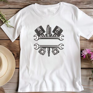 May include: White t-shirt with a black graphic of engine parts, including pistons, a spark plug, and wrenches. The design is centered on the shirt, suitable for mechanics or automotive enthusiasts.