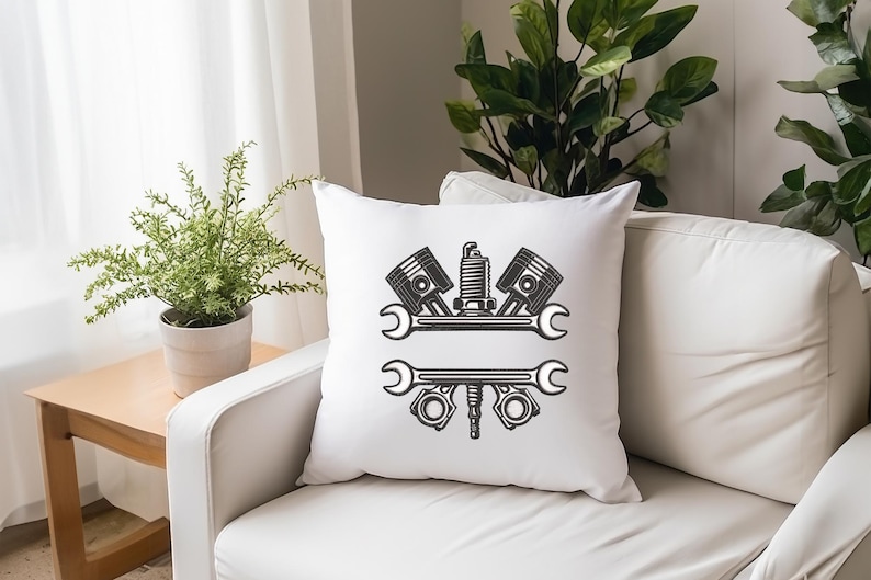 May include: White square throw pillow with a black graphic of automotive tools, including pistons, a spark plug, and wrenches. The pillow is on a white sofa, with a small wooden table and a potted plant in the background.