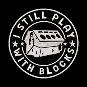 May include: Embroidered patch with the text "I STILL PLAY WITH BLOCKS" in a circular design. The design features a white image of a block structure. The patch is white on a black background.