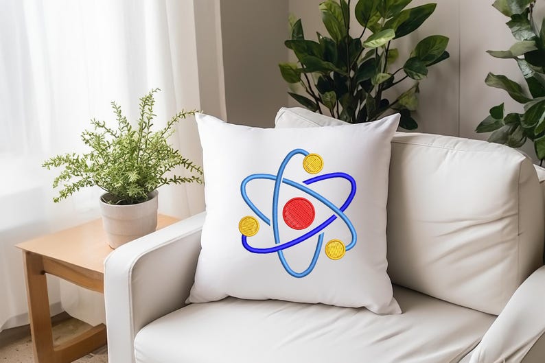 K&ouml;nnte beinhalten: Wei&szlig;es quadratisches Kissen mit einem gestickten Atom-Design. Das Atom hat eine rote Mitte, blaue Umlaufbahnen und drei gelbe kreisf&ouml;rmige Elemente. Das Kissen liegt auf einem wei&szlig;en Sofa in der N&auml;he eines kleinen Holztisches mit einer Topfpflanze.