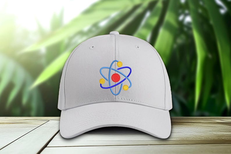 K&ouml;nnte beinhalten: Eine wei&szlig;e Baseballkappe mit einem gestickten Atom-Design. Die Atomgrafik hat einen roten Mittelpunkt, blaue Umlaufbahnen und gelbe Akzente. Die Kappe ist aus weichem Material und hat einen gebogenen Schirm.