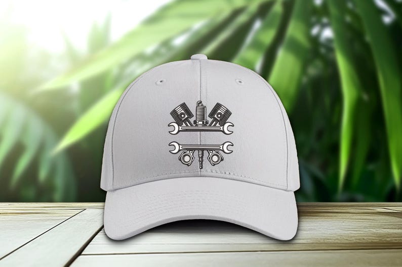May include: A white baseball cap featuring a black and gray graphic of automotive tools, including pistons, a spark plug, and wrenches. The design is centered on the front of the cap, suitable for mechanics and car enthusiasts.