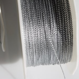 May include: Two spools of silver and black metallic thread. The thread is wound around white plastic spools.