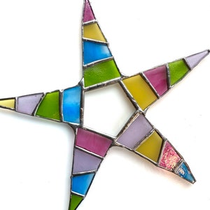 May include: A colorful stained glass star with a geometric design. The star is made of various shades of green, blue, yellow, pink, and purple glass.