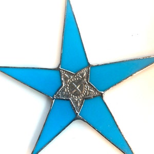 May include: A blue stained glass star with a silver center design. The star is hanging from a loop at the top.