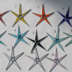 May include: Twelve stained glass star ornaments in various colors, including red, yellow, orange, blue, green, black, turquoise, and pink. Each star has a small, round, colored glass gem in the center.