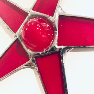 May include: A red stained glass star with a silver frame. The star has a large red circle in the center.