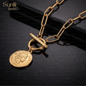 May include: Gold-coloured necklace with a coin pendant. The coin features a profile of a person and text. The necklace has a toggle clasp and a chain with oval links. The brand name "Sunlii SparkleCo" is in the top left corner.
