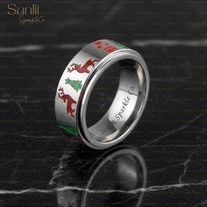 Könnte beinhalten: Ein silberner Ring mit Weihnachtsmotiven, darunter rote Rentiere, grüne Weihnachtsbäume und rote Geschenkboxen. Der Ring trägt den Schriftzug "Sunlit Sparkle Co."
