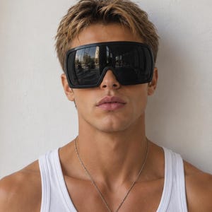May include: Oversized black shield sunglasses with a single continuous lens and a thick matte black frame, paired with a simple silver-toned rectangular pendant necklace on a thin chain and a plain white ribbed cotton tank top.
