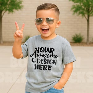 May include: A gray short-sleeved t-shirt with the text "YOUR Awesome DESIGN HERE" in black. A young person is wearing the shirt and smiling.