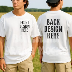 以下が含まれることがあります： 前面に「FRONT DESIGN HERE」、背面に「BACK DESIGN HERE」と書かれた白いTシャツ。Tシャツは人が着ています。その人はカーキ色のショートパンツを履いています。背景は野原です。