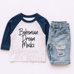 May include: A white and navy blue raglan shirt with the text "Bohemian Dream Mocks" and a pair of light blue denim shorts with distressed details. The outfit is designed for children.