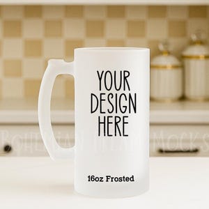 May include: A frosted glass beer mug with a handle. The mug has the text "YOUR DESIGN HERE" in black, with "16oz Frosted" below. The mug is designed for custom designs.