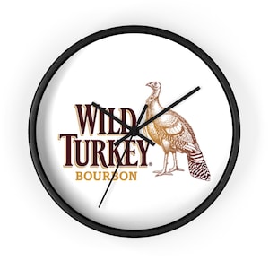 May include: Round wall clock with a black frame and a white face. The clock face features the words "WILD TURKEY BOURBON" in brown and a detailed illustration of a turkey. Black clock hands indicate the time.