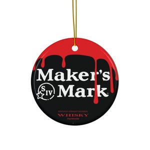 May include: A round, black and red Maker's Mark ornament with a gold string for hanging. The ornament features the Maker's Mark logo in white, with red drips along the top edge. The text "Kentucky Straight Bourbon Whisky Handmade" is printed at the bottom.
