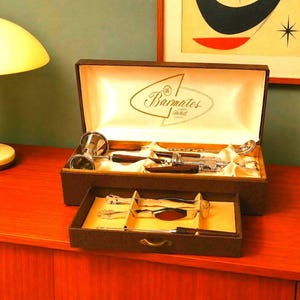 May include: A brown, two-tiered bar tool set in a presentation box labelled Barmates. The set includes silver-toned metal tools with dark wood handles, such as a jigger, bottle opener, and tongs, arranged in a satin-lined interior compartment.