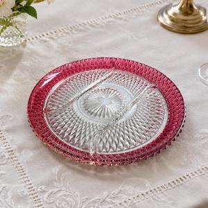 Peut inclure: Une assiette de service ronde en verre transparent divisée en sections, dotée d'un bord magenta vif avec un motif texturé en losanges. Le centre de l'assiette présente un motif clair en rayons de soleil, tandis que le bord extérieur est défini par une bordure rose foncé.