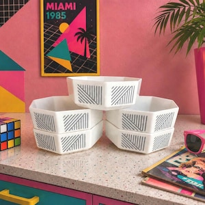 Peut inclure: Six bols géométriques blancs avec des motifs de lignes diagonales noires sont empilés sur un comptoir moucheté. Un Rubik's Cube coloré et une affiche de Miami sont en arrière-plan. Idéal pour servir.