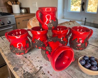 Puede incluir: Un conjunto de seis tazas de cerámica de color rojo brillante con una base texturizada de color marrón oscuro. Cada taza tiene un asa redondeada y un acabado liso y brillante en la parte superior, que contrasta con la textura rugosa y oscura de la base.