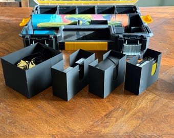 May include: A black and yellow plastic toolbox with multiple compartments, open to reveal colorful rolled items. Several black card holders and a black box are arranged in front of the toolbox on a wooden surface.