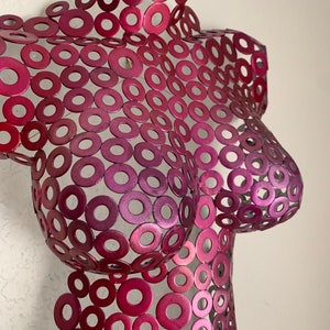 May include: A pink metal sculpture of a torso made from many small circles.