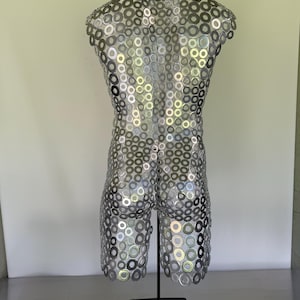 May include: A silver metal sculpture of a torso and legs, constructed from numerous circular washers. The sculpture is mounted on a black metal stand, showcasing a unique industrial design. The piece is displayed against a neutral background.