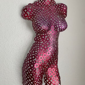 May include: A pink metal sculpture of a torso made from many small circles.