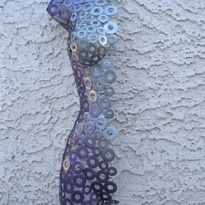 May include: A metal sculpture of a human torso made from a collection of washers. The washers are arranged in a pattern that creates the shape of a body. The washers are painted in shades of purple and silver.