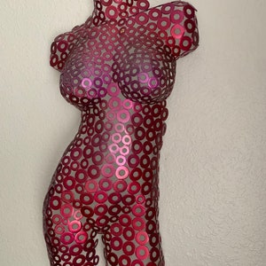 May include: A red metal sculpture of a torso made from many small circles.