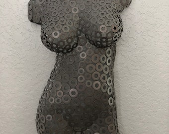 May include: A metal sculpture of a torso made from hundreds of small metal washers. The sculpture is painted a dark gray color and has a smooth, rounded surface.
