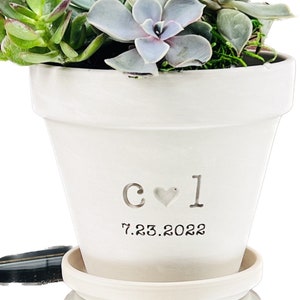 May include: White ceramic planter with a heart and initials "C ♥ I" and the date "7.23.2022" engraved on the side. The planter is filled with a variety of succulents.