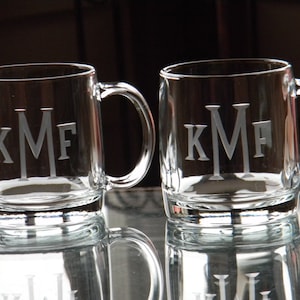 May include: Two clear glass mugs with handles, each engraved with the monogram "KMF".