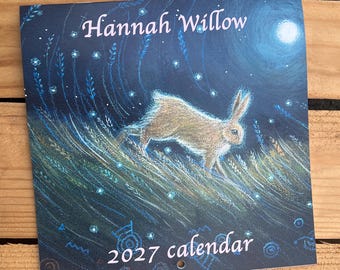 Puede incluir: Un calendario cuadrado de 2027 con una escena nocturna en azul oscuro que muestra un conejo marrón corriendo entre hierba alta. La ilustración incluye una luna brillante, puntos de luz y el texto Hannah Willow arriba y 2027 calendar abajo.