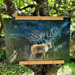 May include: A black and white drawing of a deer with a large, intricate antler structure made of branches and leaves. The deer is standing in a field of tall grass with a small rabbit in the foreground. The background is a dark blue sky with stars and a crescent moon.