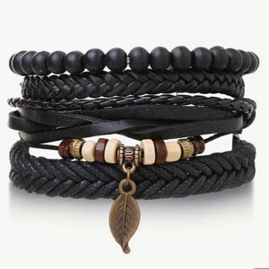 May include: A set of five black leather and braided bracelets with a wooden bead and leaf charm. The bracelets are layered and feature different textures.