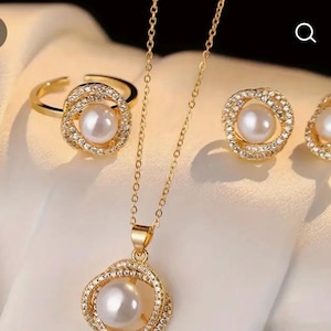 以下が含まれることがあります： ゴールドトーンのジュエリーセット。リング、ネックレス、イヤリングが含まれています。各アイテムは、小さな輝くクリスタルで囲まれた中央の白い真珠が特徴です。リングは調整可能で、ネックレスは繊細なチェーンが付いています。
