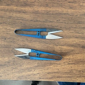 May include: Two blue and silver small scissors with pointed tips. The scissors are on a wooden surface.