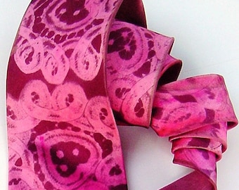 May include: A pink and burgundy patterned silk tie with a paisley design. The tie is folded and tied in a knot.