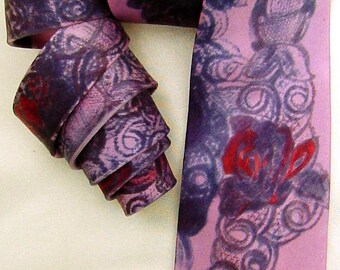 May include: A pink silk tie with a dark purple and red floral pattern. The tie is folded and tied in a knot.