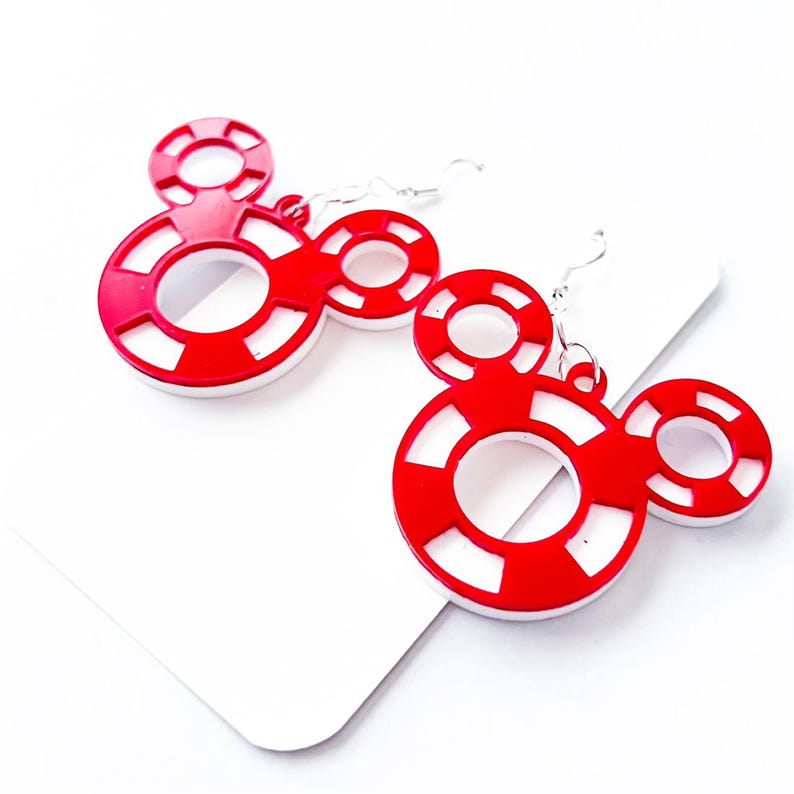 May include: A pair of red and white Mickey Mouse-shaped earrings. The earrings feature a red outline with white stripes and a white inner circle. The earrings hang from silver-colored hooks.