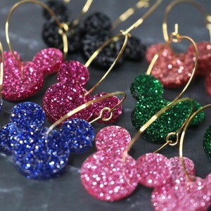 May include: A set of gold hoop earrings with glitter Mickey Mouse head charms in pink, blue, and green.